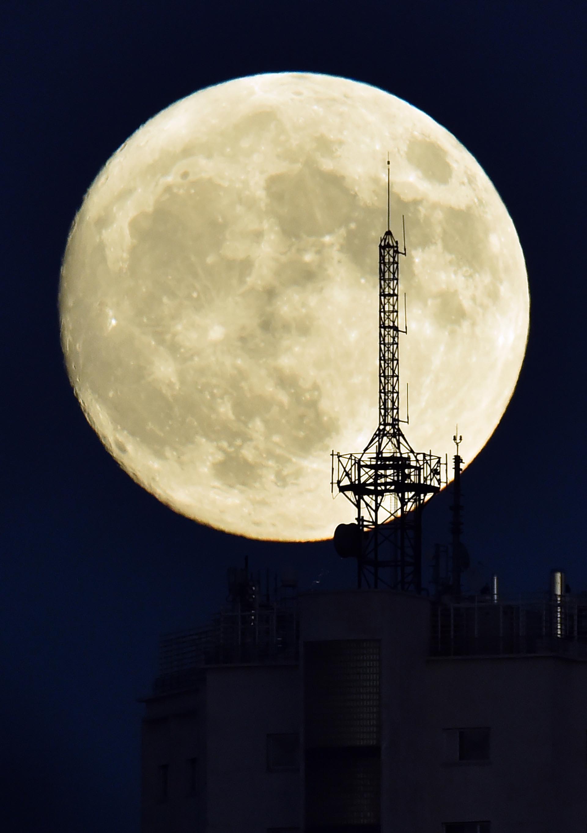 The moon rises over an antenna on the top of a building in Madrid on November 13, 2016, on the eve of a "supermoon". On November 14, 2016, the moon will orbit closer to the earth than at any time since 1948, named a 'supermoon', it is defined by a Full or New moon coinciding with the moon's closest approach to the Earth. / AFP PHOTO / GERARD JULIEN