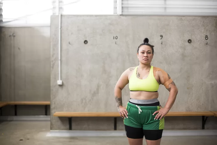 Portrait Of Female Rugby Player In Sports Bra And Shorts Standing In Changing Rooms Looking Into Lens