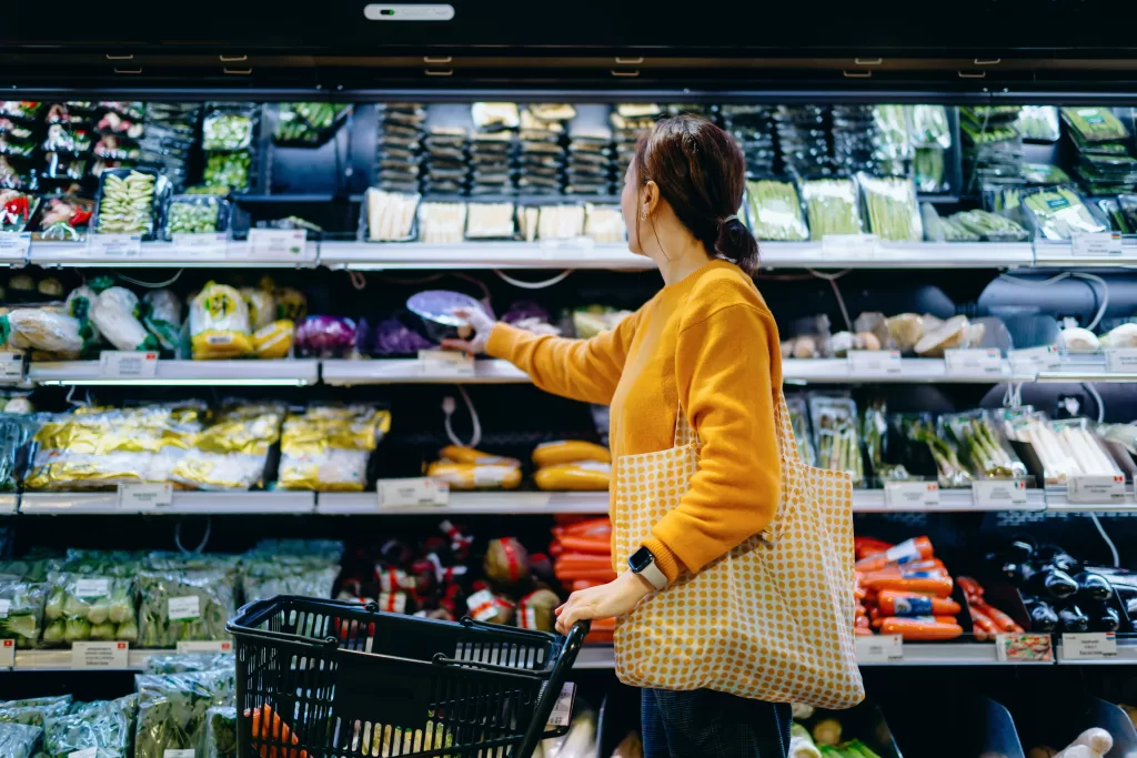 Young Asian Woman With Shopping Cart, Carrying A Reusable Shopping Bag, Shopping For Fresh Organic Fruits And Vegetables In Supermarket. Environmentally Friendly Concept. Zero Waste And Plastic Free. Eco Friendly Shopping. Sustainable Living Lifestyle